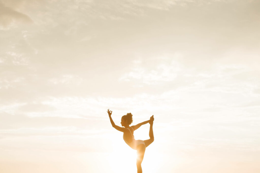 Frau macht eine Yogaübung, Sonnenuntergang im Hinterrund